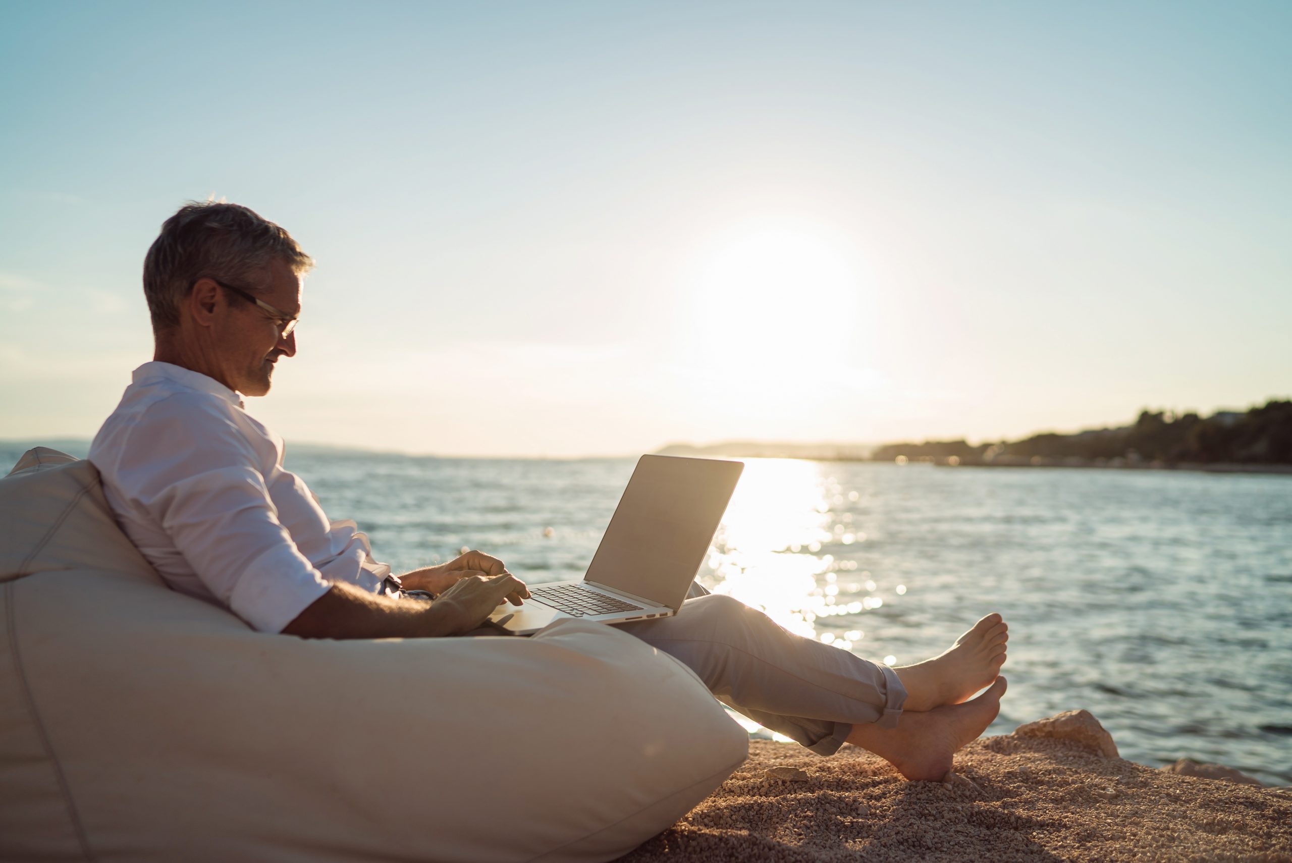 Управление из любой точки. Бизнесмен на пляже с ноутбуком. Счастливый бизнесмен на пляже. Человек на лежаке. Мужчина на пляже с ноутбуком.